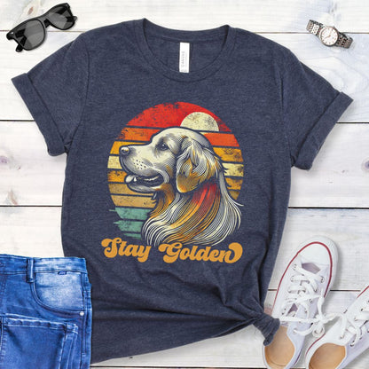Heather navy t-shirt with 'Stay Golden' text and a vintage sunset graphic with a line drawn Golden Retriever, presented on a wooden surface with jeans and shoes.