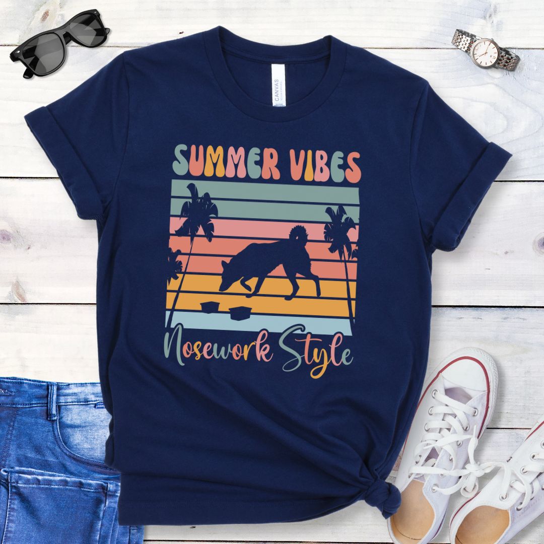 Navy t-shirt with vintage sunset, sniffing dog and text 'Summer Vibes Nosework Style' design on a wooden surface with jeans and shoes.