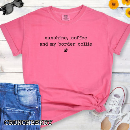 Pink Comfort Colors t-shirt for Border Collie dog lovers with 'sunshine, coffee, and my border collie' text in minimalist typewriter lettering and paw print, shown on a wooden surface with accessories.