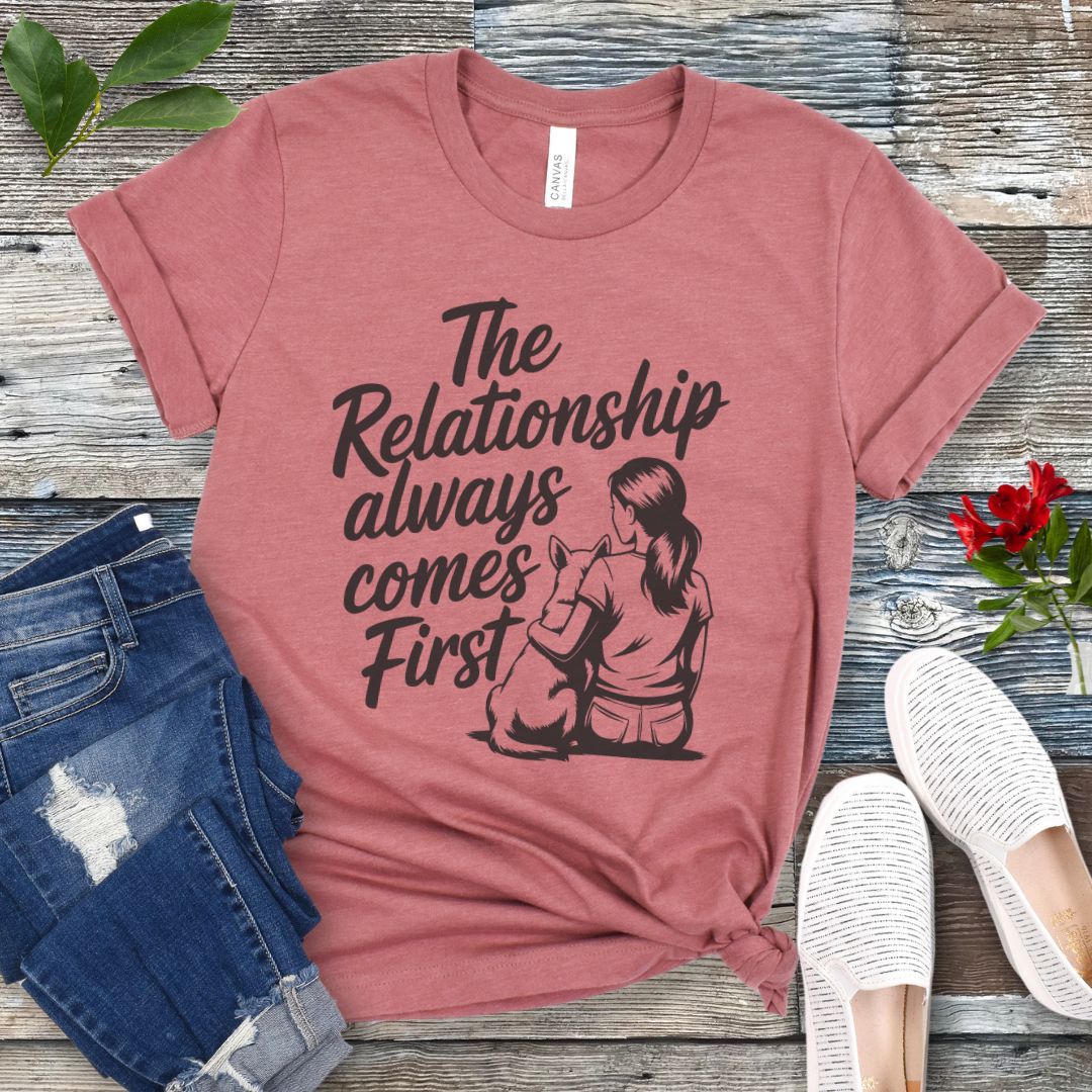 A mauve t-shirt for dog lovers and dog trainers with an illustration of a girl sitting with her dog, and the text 'The Relationship always comes First', displayed with jeans and shoes.