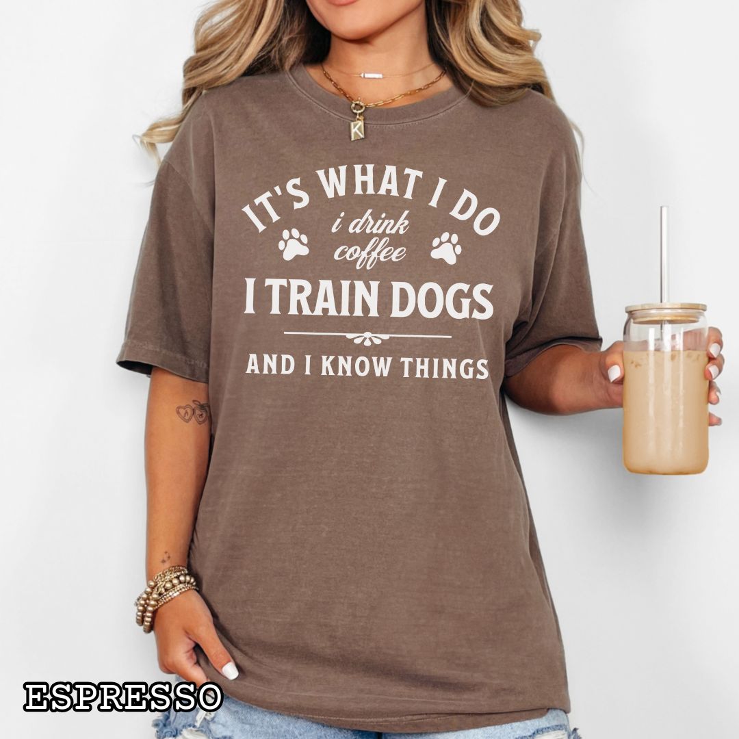 Person wearing a brown (Espresso) Comfort Colors dog training t-shirt with a humorous dog trainer quote, 'It's what I do, I drink coffee, I train dogs and I know things' holding a coffee cup.