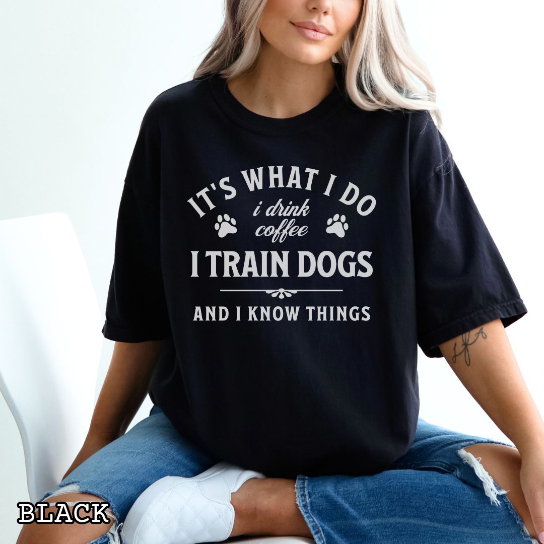 Person wearing a black Comfort Colors dog training t-shirt with text and paw prints, sitting on a white couch.