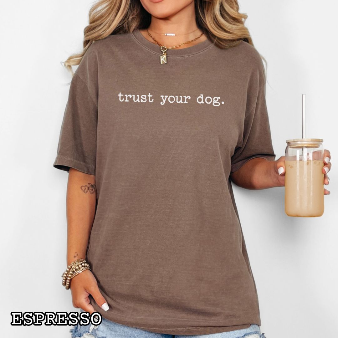 Brown (Espresso) Comfort Colors t-shirt with 'trust your dog.' text, presented on a wooden surface with shoes and jeans.