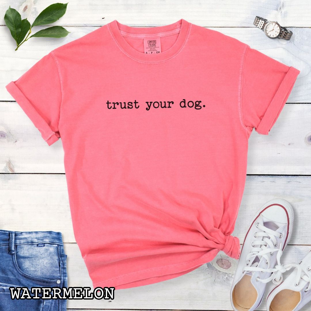 Pink (Watermelon)) Comfort Colors t-shirt with 'trust your dog.' text, presented on a wooden surface with shoes and jeans.