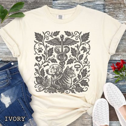 Beige Comfort Colors Veterinary Medicine t-shirt with a monochrome linocut style design of a dog, a cat, and various veterinary and botanical elements, shown on a wooden surface with jeans and shoes.