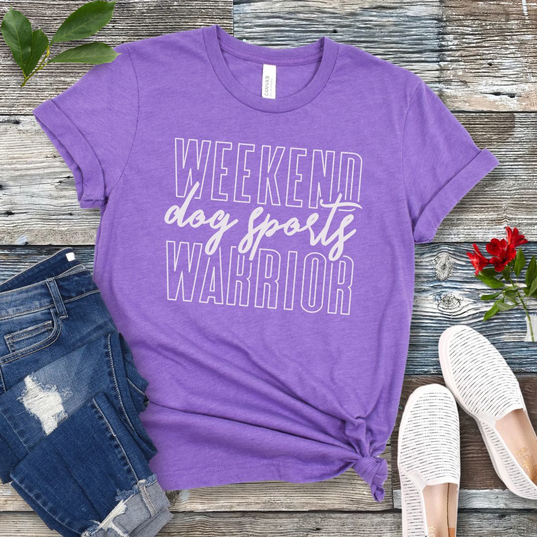 A purple dog training t-shirt with the text 'Weekend dog sports warrior' printed in white, displayed flat with a pair of blue jeans and white shoes.