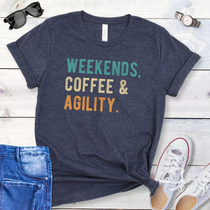 Heather navy dog sports t-shirt with 'Weekends, Coffee & Agility' in bold, colorful text, presented on a wooden surface with jeans and shoes.