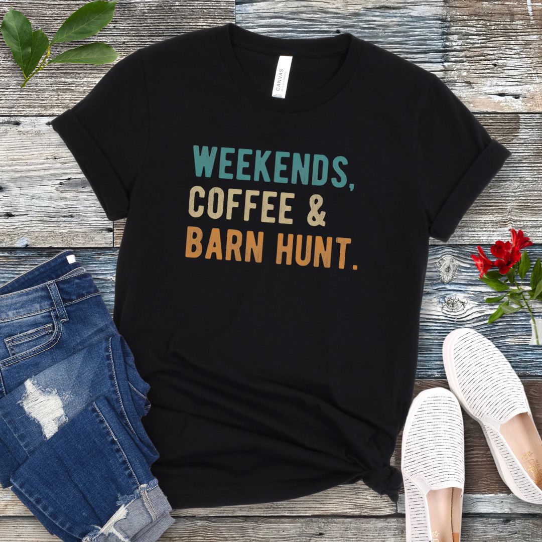 Black dog sports t-shirt with 'Weekends, Coffee & Barn Hunt' in bold, colorful text, presented on a wooden surface with jeans and shoes.