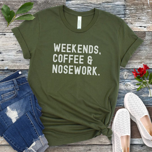 Military green t-shirt with 'Weekends, Coffee & Nosework' text on a wooden surface with jeans and shoes.