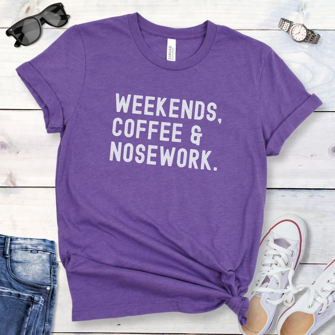 Purple dog sports t-shirt with 'Weekends, Coffee & Nosework' text on a wooden surface with jeans and shoes.