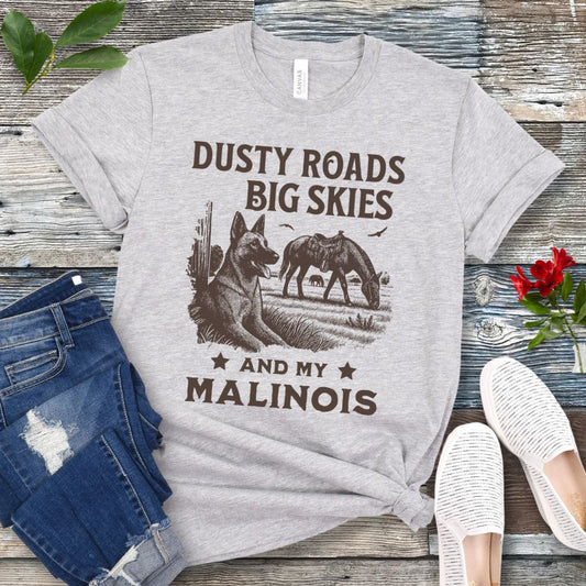 Gray t-shirt with graphic of Malinois in a rural scene and quote on a wooden surface with jeans and shoes.