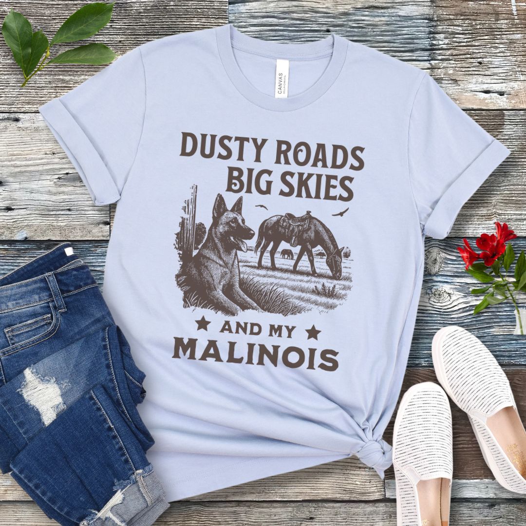 Light blue t-shirt with graphic of Malinois in a rural scene and quote on a wooden surface with jeans and shoes.