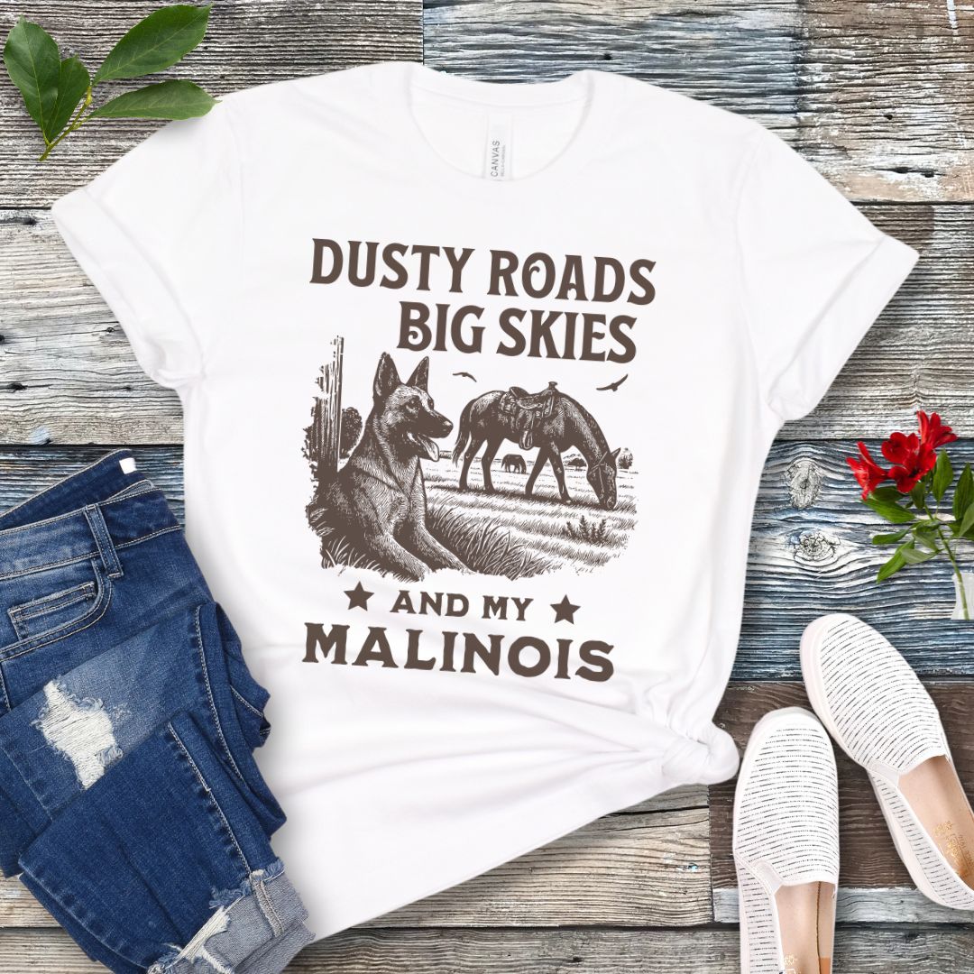 White t-shirt with graphic of Malinois in a Western scene and quote on a wooden surface with jeans and shoes.