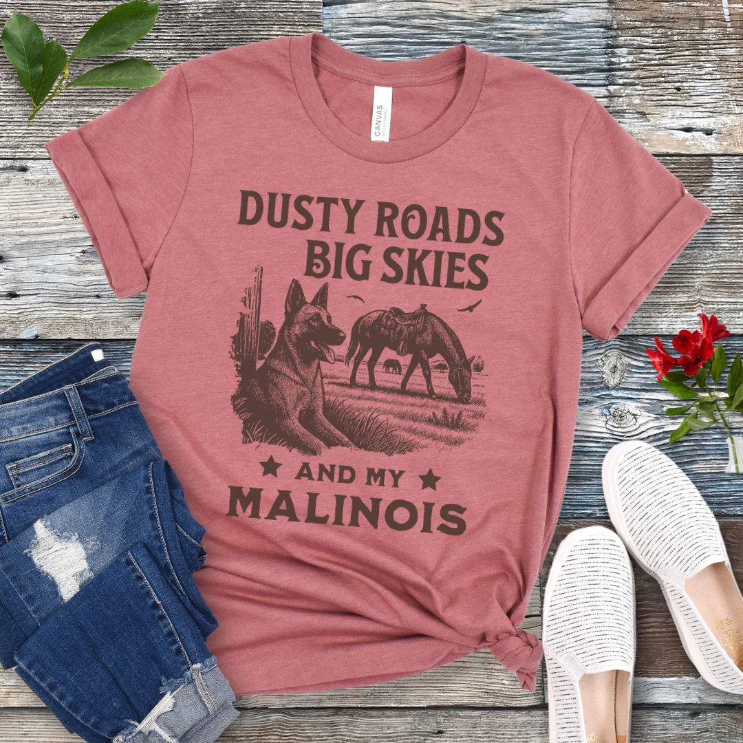 Mauve t-shirt with graphic of Malinois in a Western scene and quote on a wooden surface with jeans and shoes.
