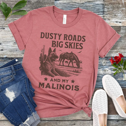 Mauve t-shirt with graphic of Malinois in a Western scene and quote on a wooden surface with jeans and shoes.