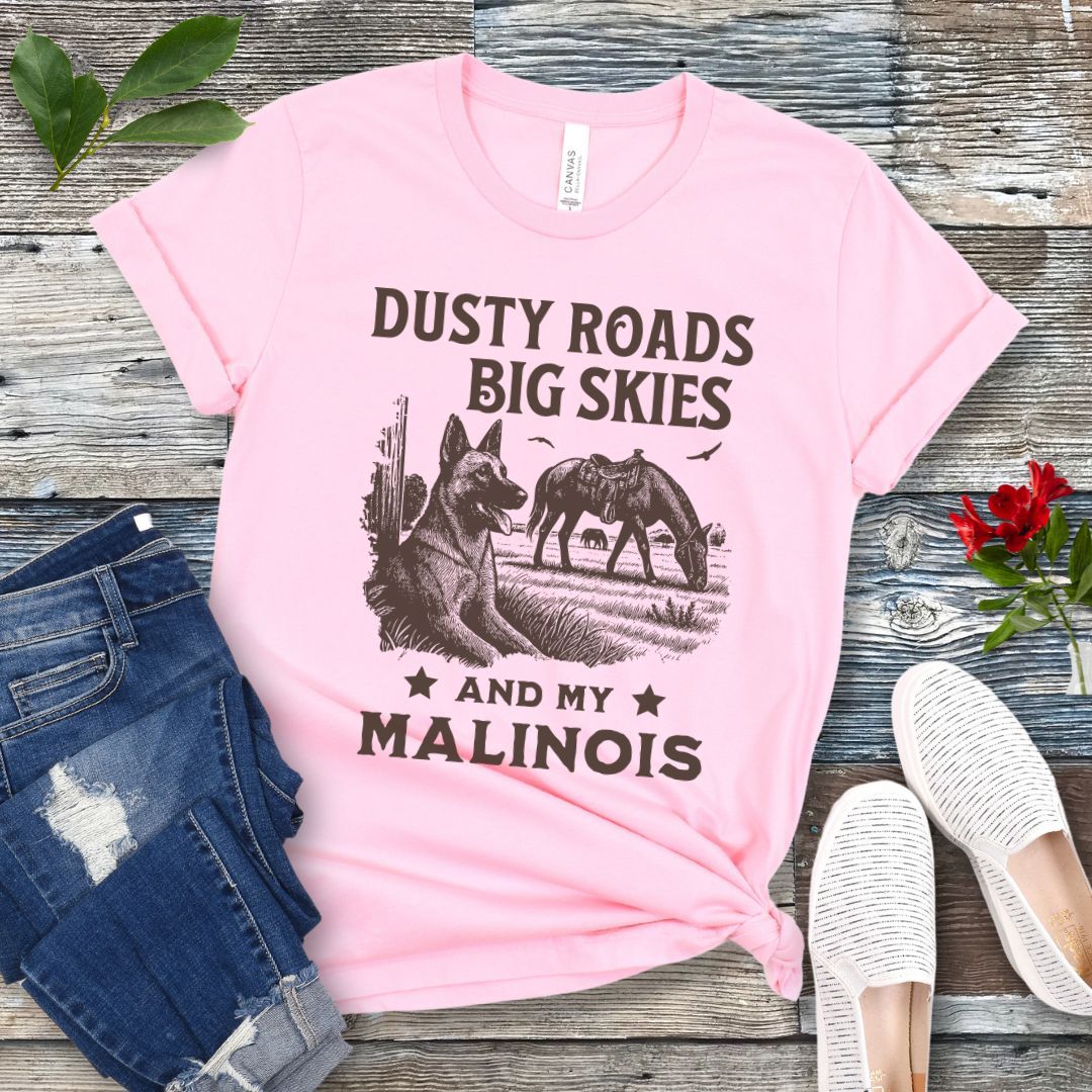 Pink t-shirt with graphic of Malinois in a Western scene and quote on a wooden surface with jeans and shoes.