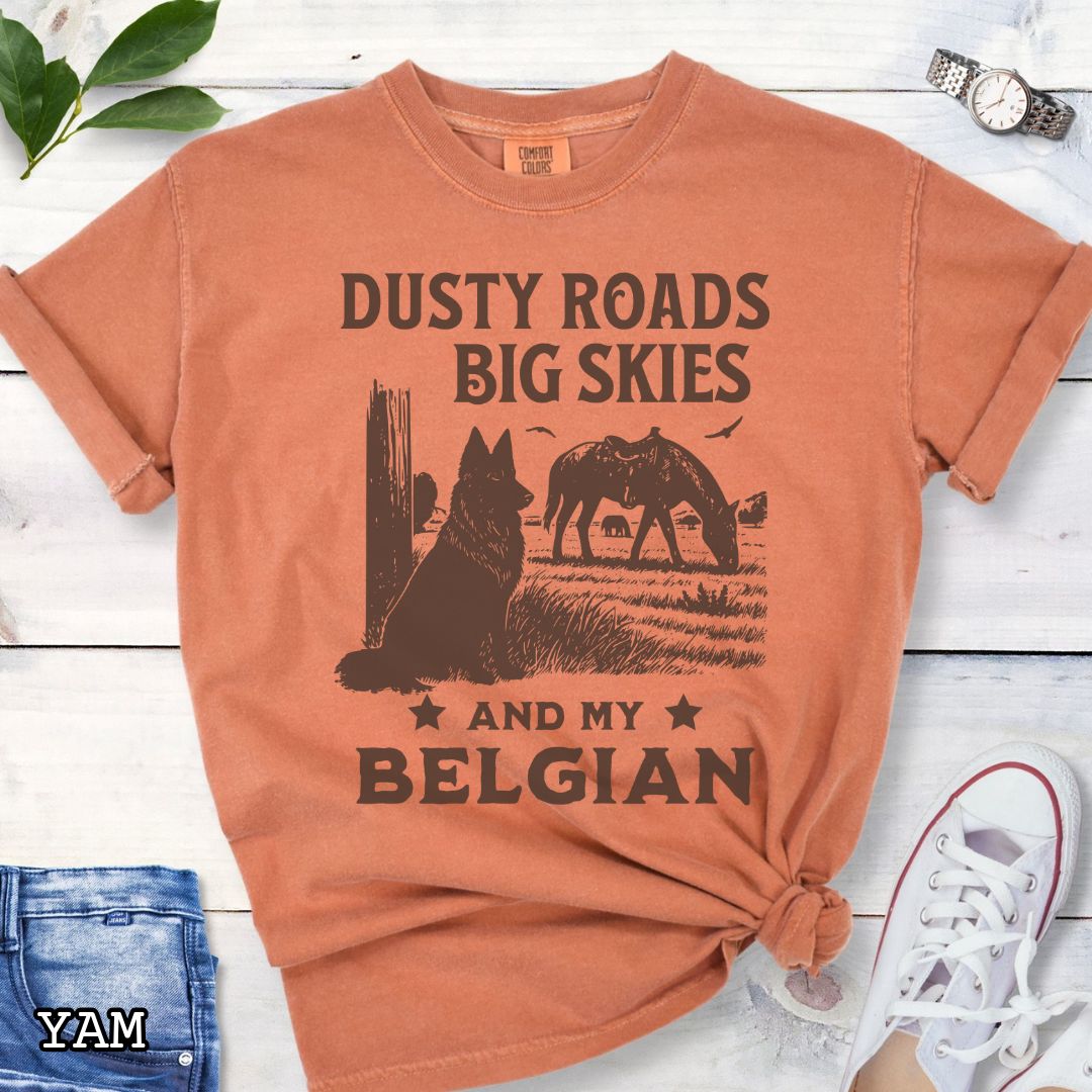 Orange Comfort Colors t-shirt featuring a Western-style design with grazing horse, rustic fence, and a Belgian Sheepdog illustration; text reads “Dusty Roads, Big Skies, and My Belgian.”