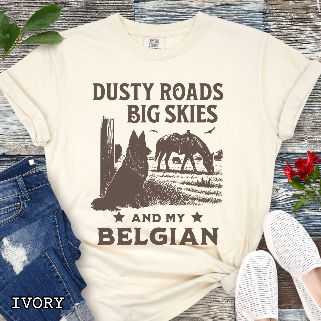 Beige Comfort Colors t-shirt featuring a Western-style design with grazing horse, rustic fence, and a Belgian Sheepdog illustration; text reads “Dusty Roads, Big Skies, and My Belgian.”