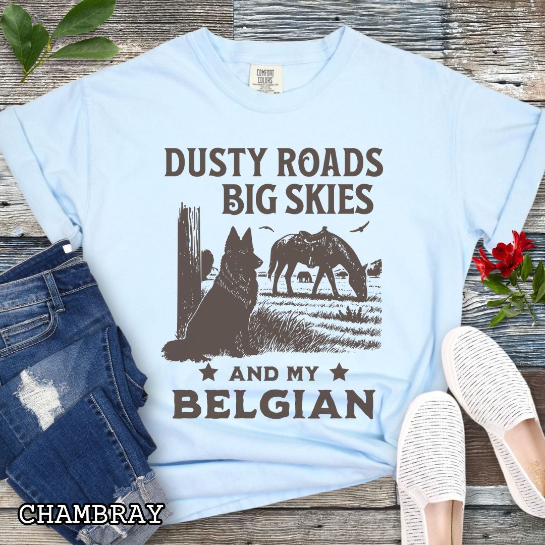 Light blue Comfort Colors t-shirt featuring a Western-style design with grazing horse, rustic fence, and a Belgian Sheepdog illustration; text reads “Dusty Roads, Big Skies, and My Belgian.”