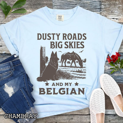 Light blue Comfort Colors t-shirt featuring a Western-style design with grazing horse, rustic fence, and a Belgian Sheepdog illustration; text reads “Dusty Roads, Big Skies, and My Belgian.”