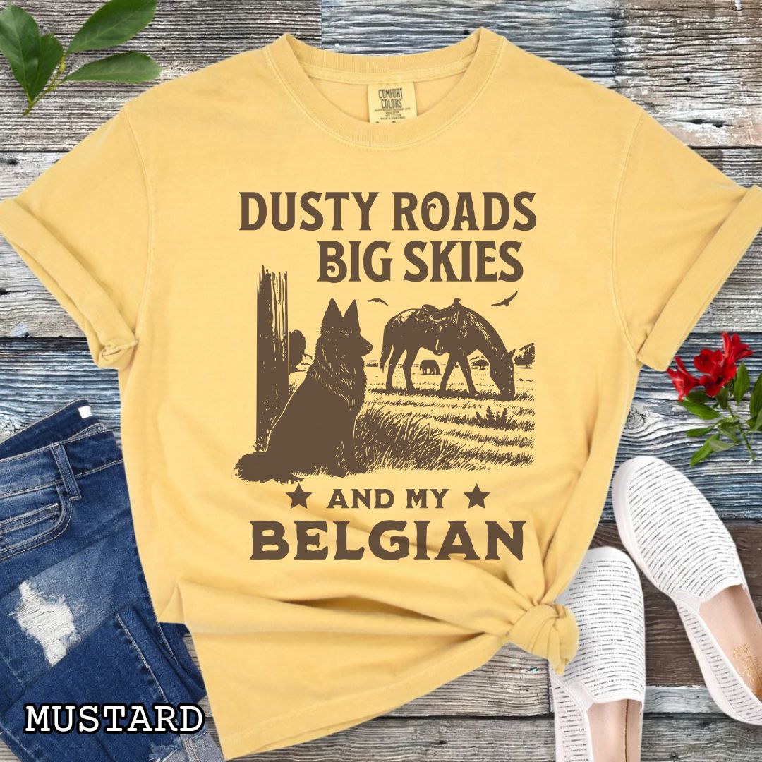 Mustard-yellow Comfort Colors t-shirt featuring a Western-style design with grazing horse, rustic fence, and a Belgian Sheepdog illustration; text reads “Dusty Roads, Big Skies, and My Belgian.”