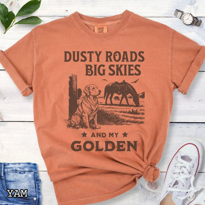 Yam-orange Comfort Colors t-shirt featuring a Western-style design with grazing horse, rustic fence, and a Golden Retriever illustration; text reads “Dusty Roads, Big Skies, and My Golden.”