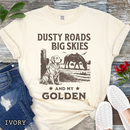 Ivory Comfort Colors t-shirt featuring a Western-style design with grazing horse, rustic fence, and a Golden Retriever illustration; text reads “Dusty Roads, Big Skies, and My Golden.”