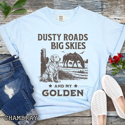 Light blue Comfort Colors t-shirt featuring a Western-style design with grazing horse, rustic fence, and a Golden Retriever illustration; text reads “Dusty Roads, Big Skies, and My Golden.”