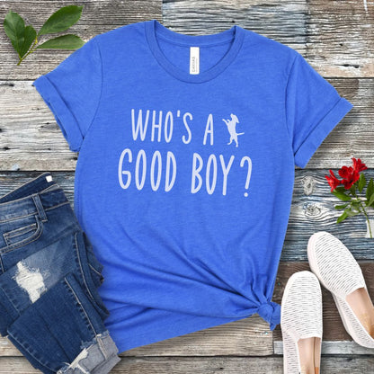 Royal blue unisex t-shirt with 'WHO'S A GOOD BOY? in playful font and jumping dog, presented on a wooden surface with jeans and shoes.