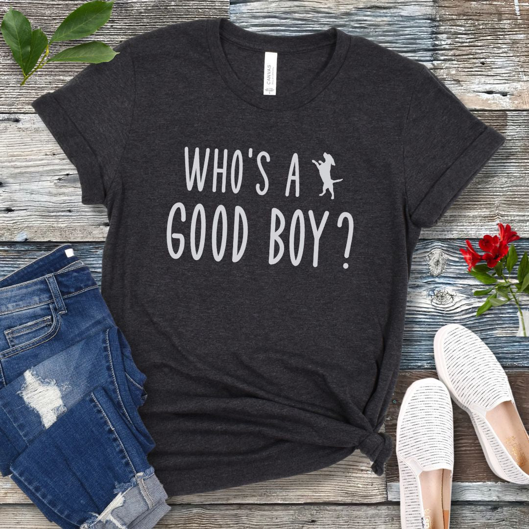 Dark Grey unisex t-shirt with 'WHO'S A GOOD BOY? in playful font and jumping dog, presented on a wooden surface with jeans and shoes.