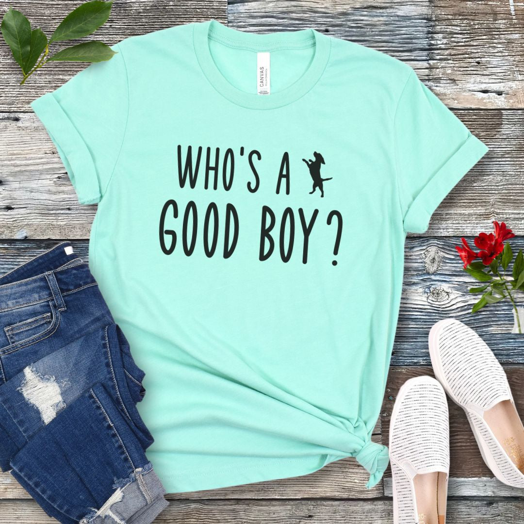 Mint green unisex t-shirt with 'WHO'S A GOOD BOY? in playful font and jumping dog, presented on a wooden surface with jeans and shoes.