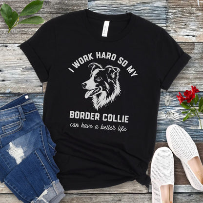 Black unisex t-shirt for Border Collie lovers with breed graphic and humorous text 'I work hard so my Border Collie can have a better life', shown on a wooden surface with jeans and shoes. 