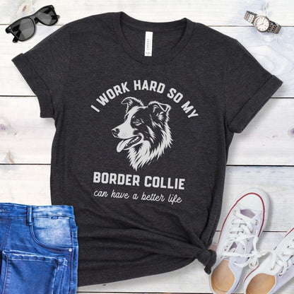 Dark grey unisex t-shirt for Border Collie lovers with breed graphic and humorous text 'I work hard so my Border Collie can have a better life', shown on a wooden surface with jeans and shoes. 