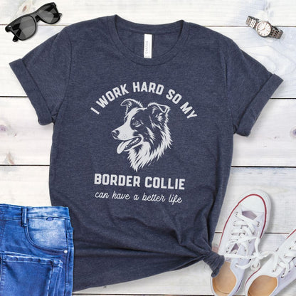 Heather navy blue unisex t-shirt for Border Collie lovers with breed graphic and humorous text 'I work hard so my Border Collie can have a better life', shown on a wooden surface with jeans and shoes. 