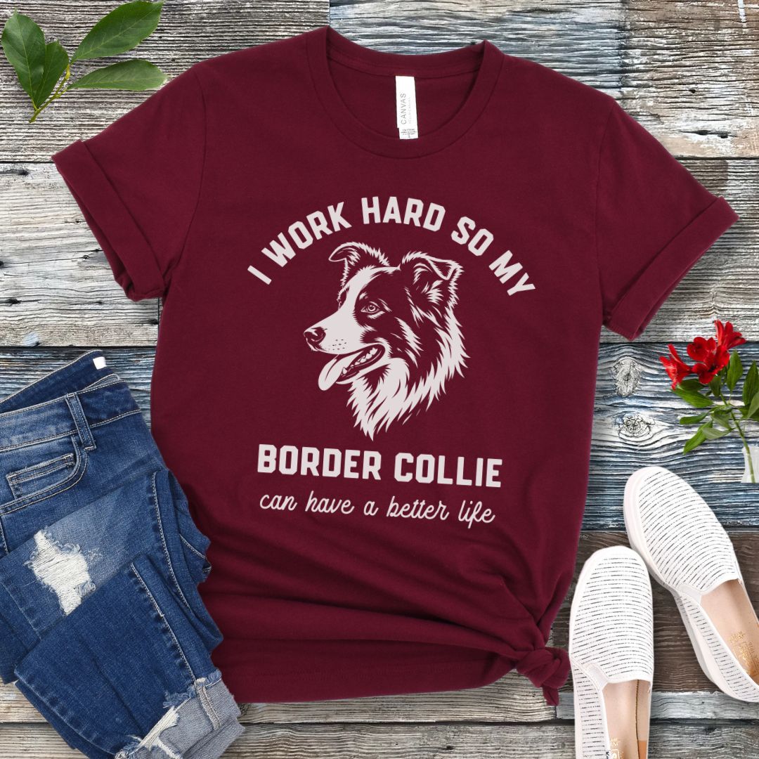 Maroon unisex t-shirt for Border Collie lovers with breed graphic and humorous text 'I work hard so my Border Collie can have a better life', shown on a wooden surface with jeans and shoes. 